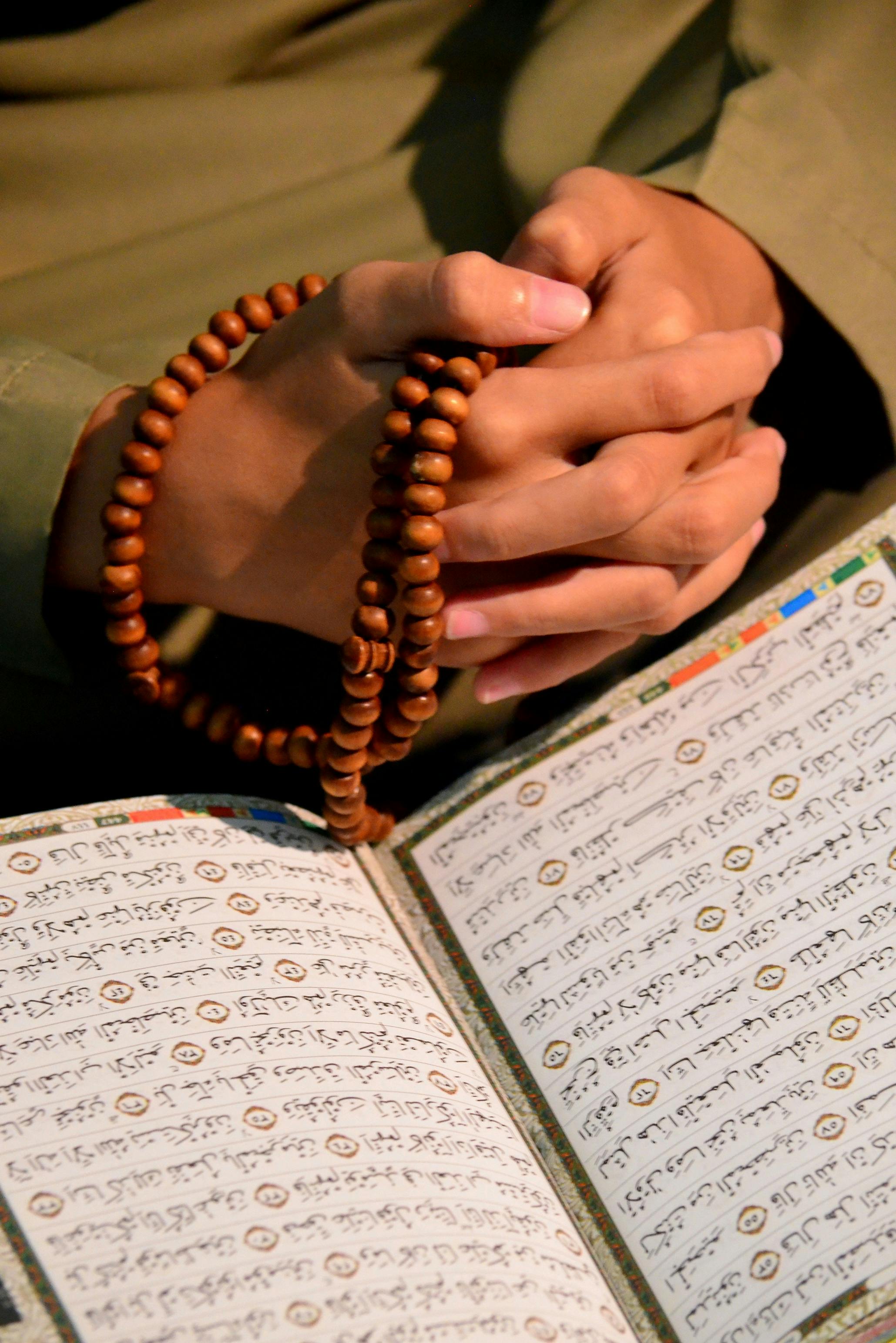 Hands holding tasbeeh over an open Qur'an